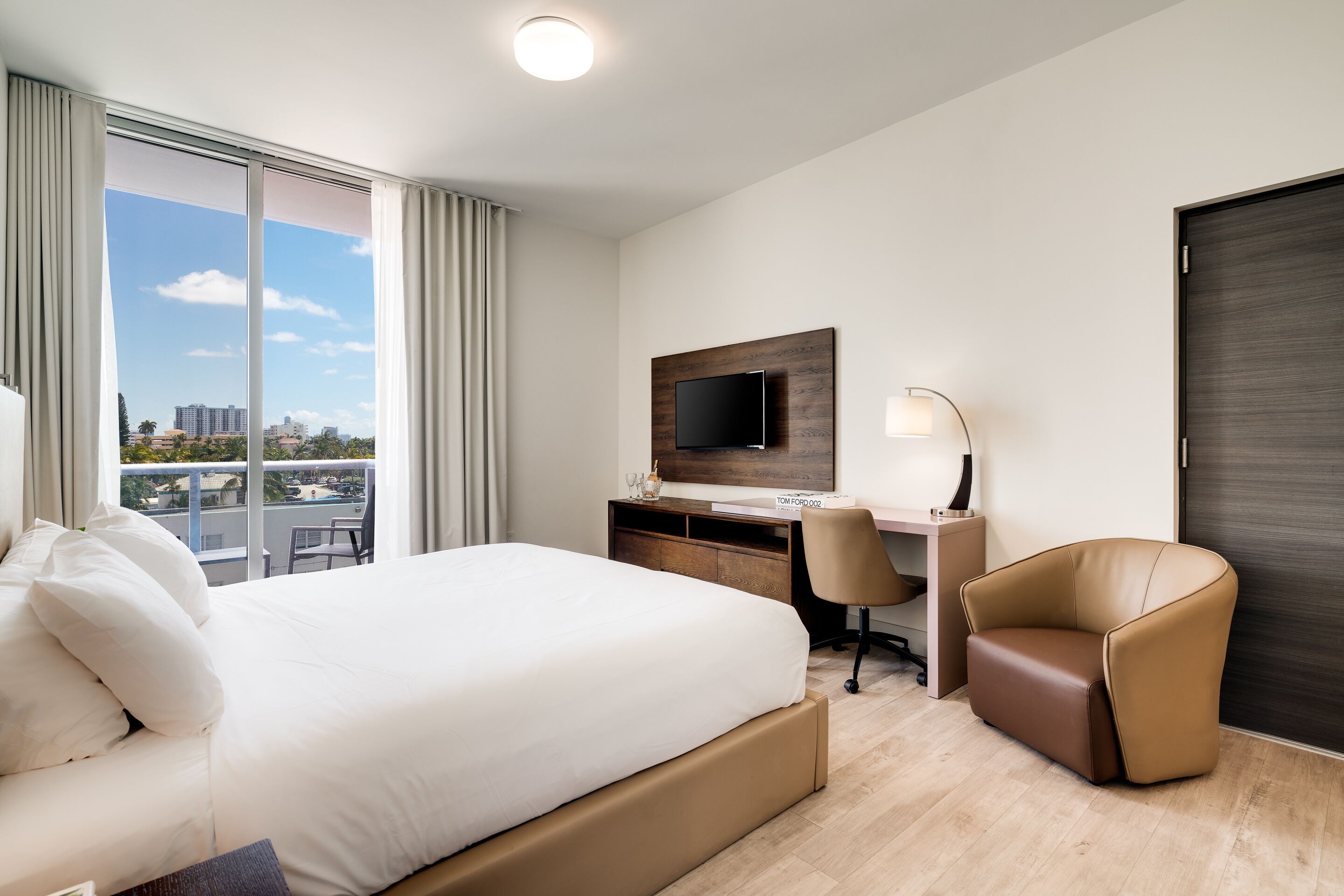 A hotel room with a large bed, a desk with a computer, a chair, and a TV on the wall.