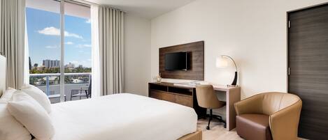 A hotel room with a large bed, a desk with a computer, a chair, and a TV on the wall.