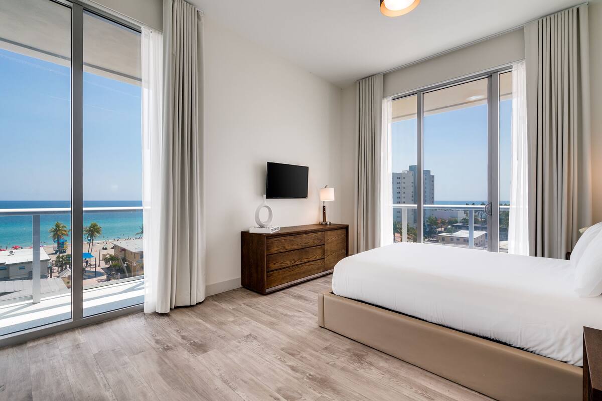Une chambre d’hôtel avec un grand lit, une télévision, une commode et une vue sur la plage et la ville.