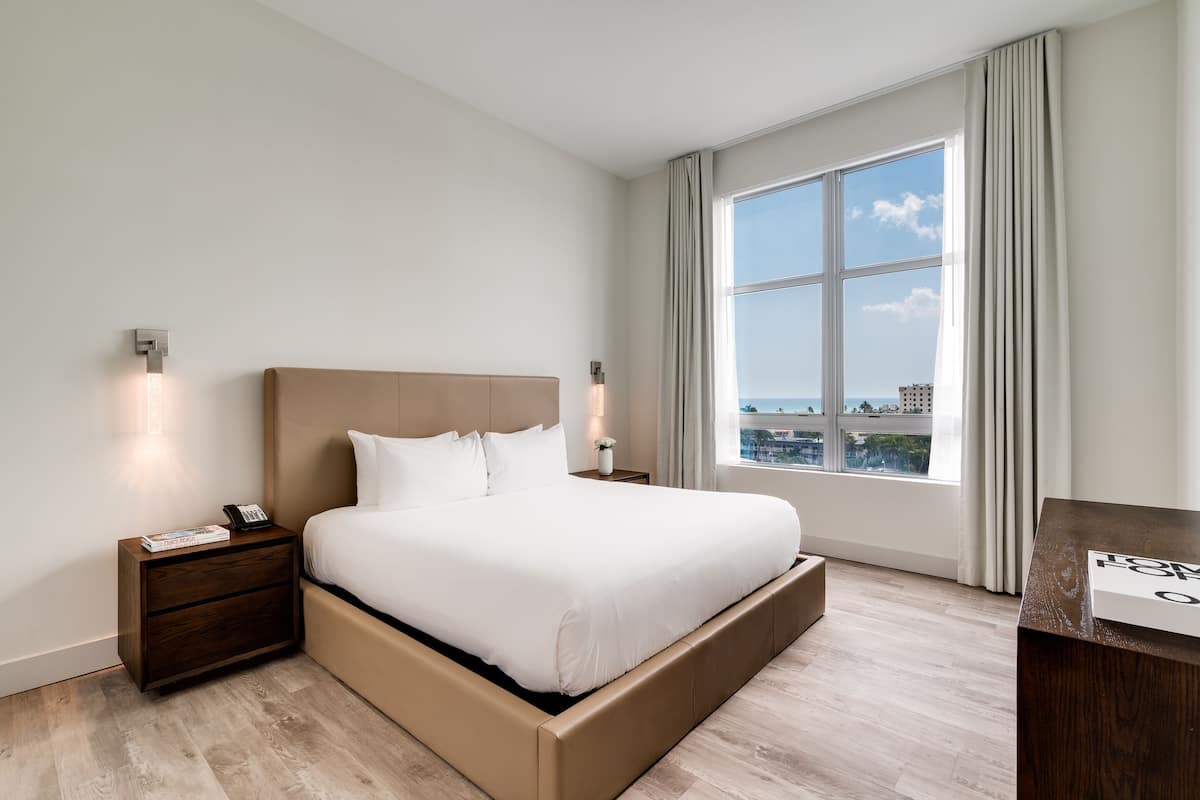 Une chambre d’hôtel moderne dotée d’un grand lit, d’une table de chevet, d’un bureau et d’une fenêtre donnant sur la ville.