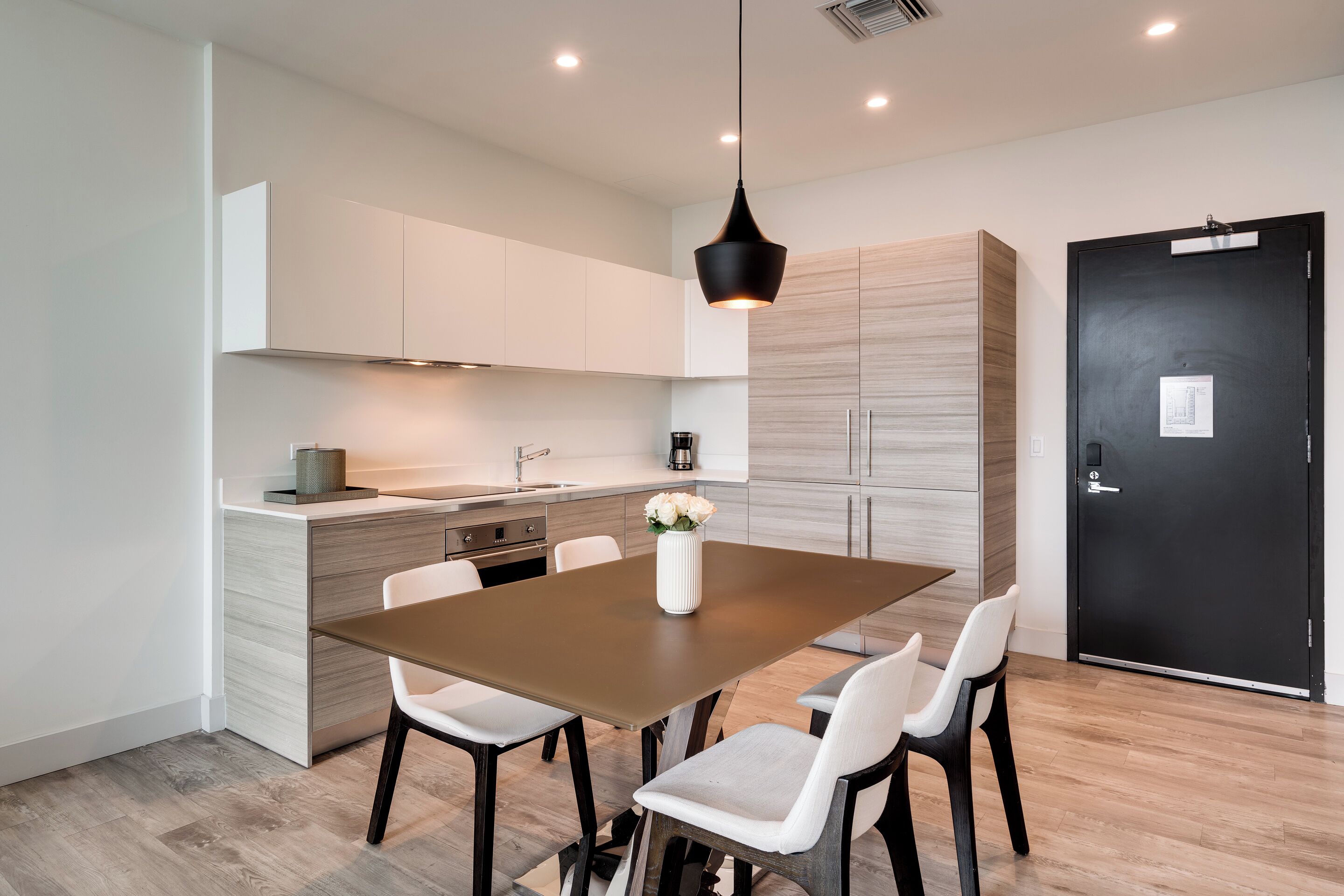 A modern kitchen with a central island, white cabinets, and a black door.