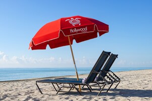 Una sombrilla con la marca "Hollywood Florida", dos sillas de playa y una vista despejada del océano.