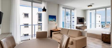 A modern hotel room with a balcony, a dining area, a sofa, and a TV.