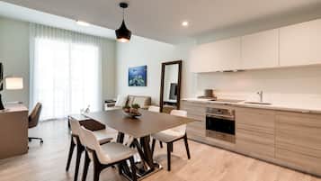 A modern kitchen with a dining area, featuring a wooden table, white chairs, and a large window with sheer curtains.