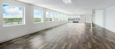 Amplia habitación de hotel, bien iluminada, con ventanas grandes, suelo de madera y una lámpara de araña moderna.