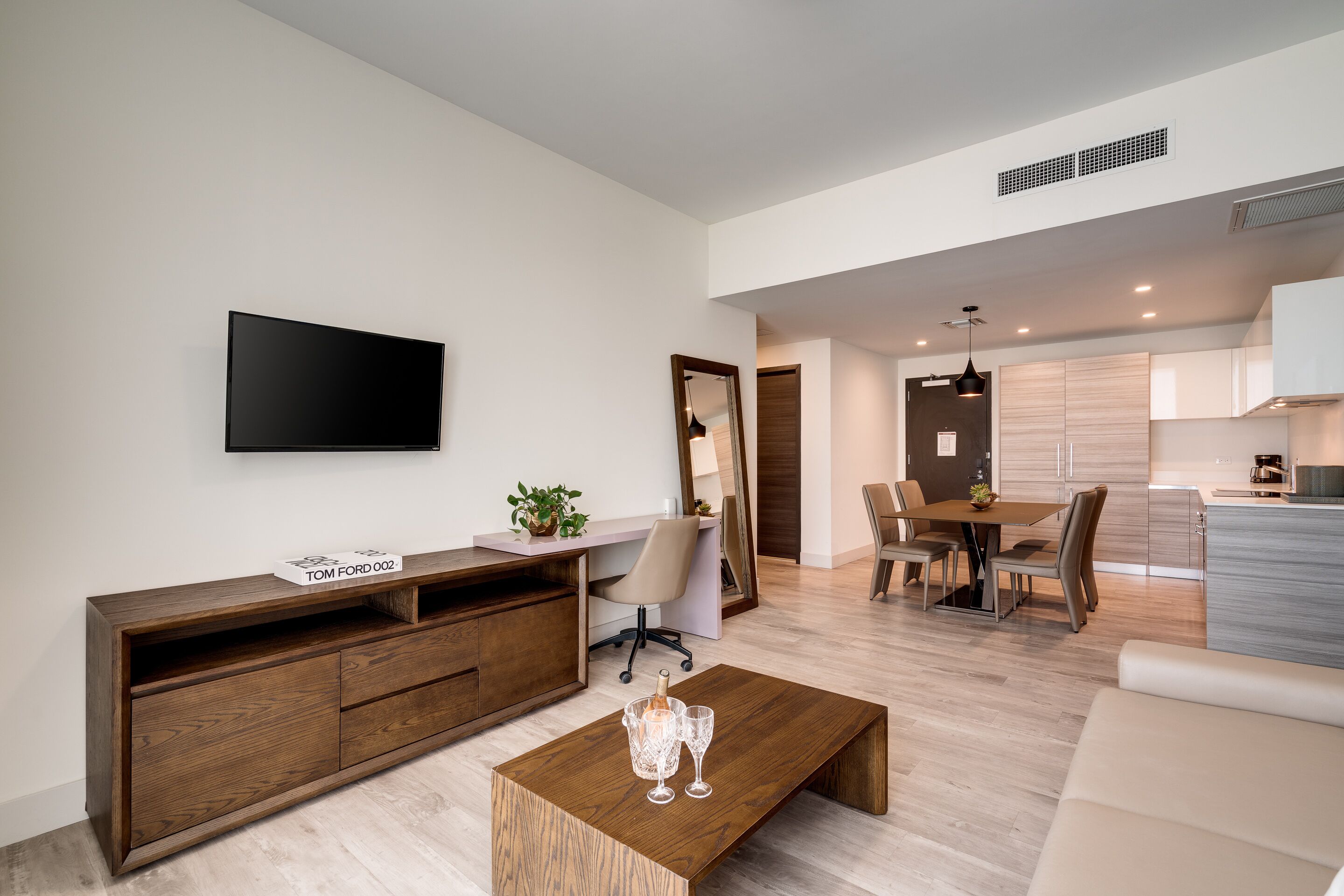 A modern living room with a flat-screen TV, wooden entertainment unit, and a coffee table with glasses.