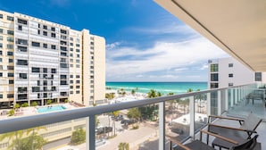 A balcony with a view of the ocean, a swimming pool, and adjacent buildings.