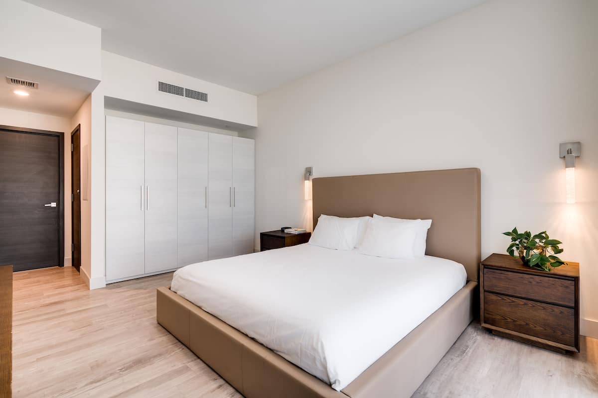 Une chambre moderne avec un grand lit, une armoire et une table de chevet agrémentée d’une plante.