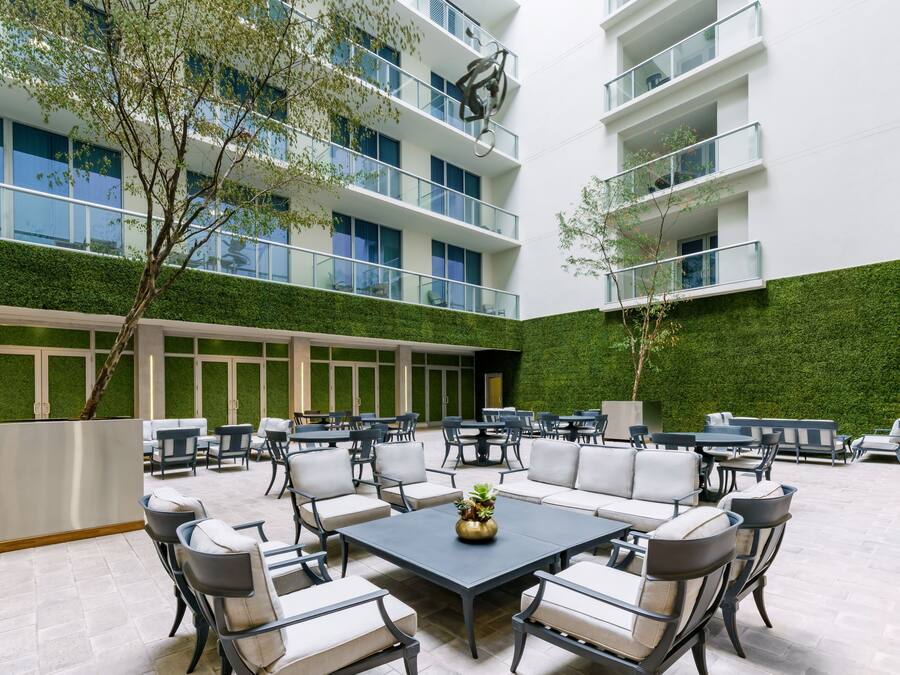 Un patio exterior moderno con varias zonas de estar, una mesa central y una pared verde.