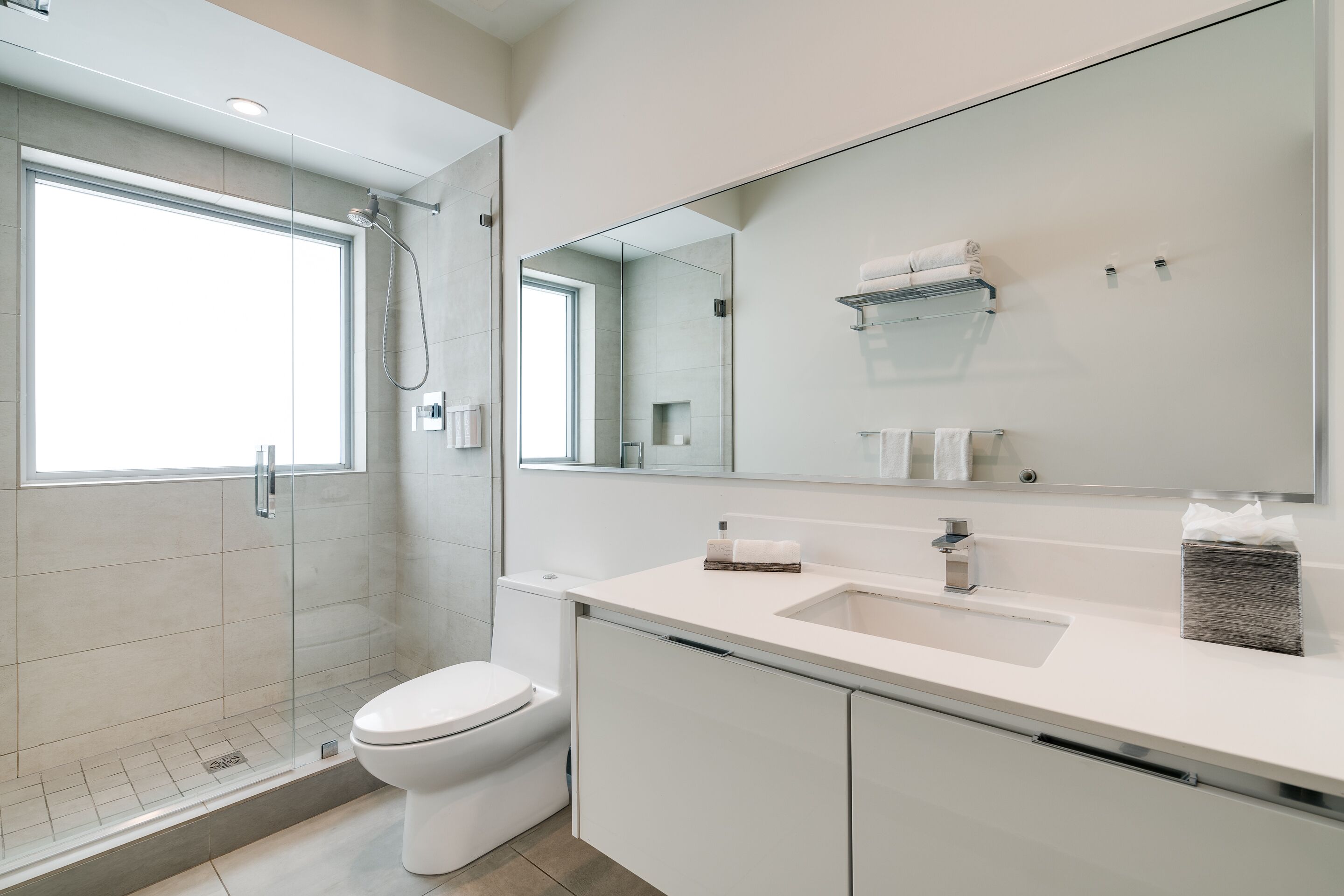 Een moderne badkamer met een glazen douchecabine, toilet, wastafel met spiegel en een handdoekrek.