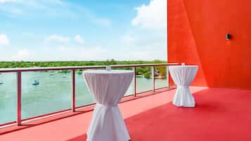A balcony with two white tables, a red floor, and a view of boats on water.