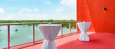 A balcony with two white tables, a red floor, and a view of boats on water.