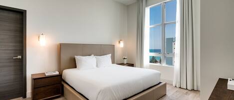 A modern hotel room with a large bed, two bedside tables, a nightstand, a window with curtains, and a view of the city.