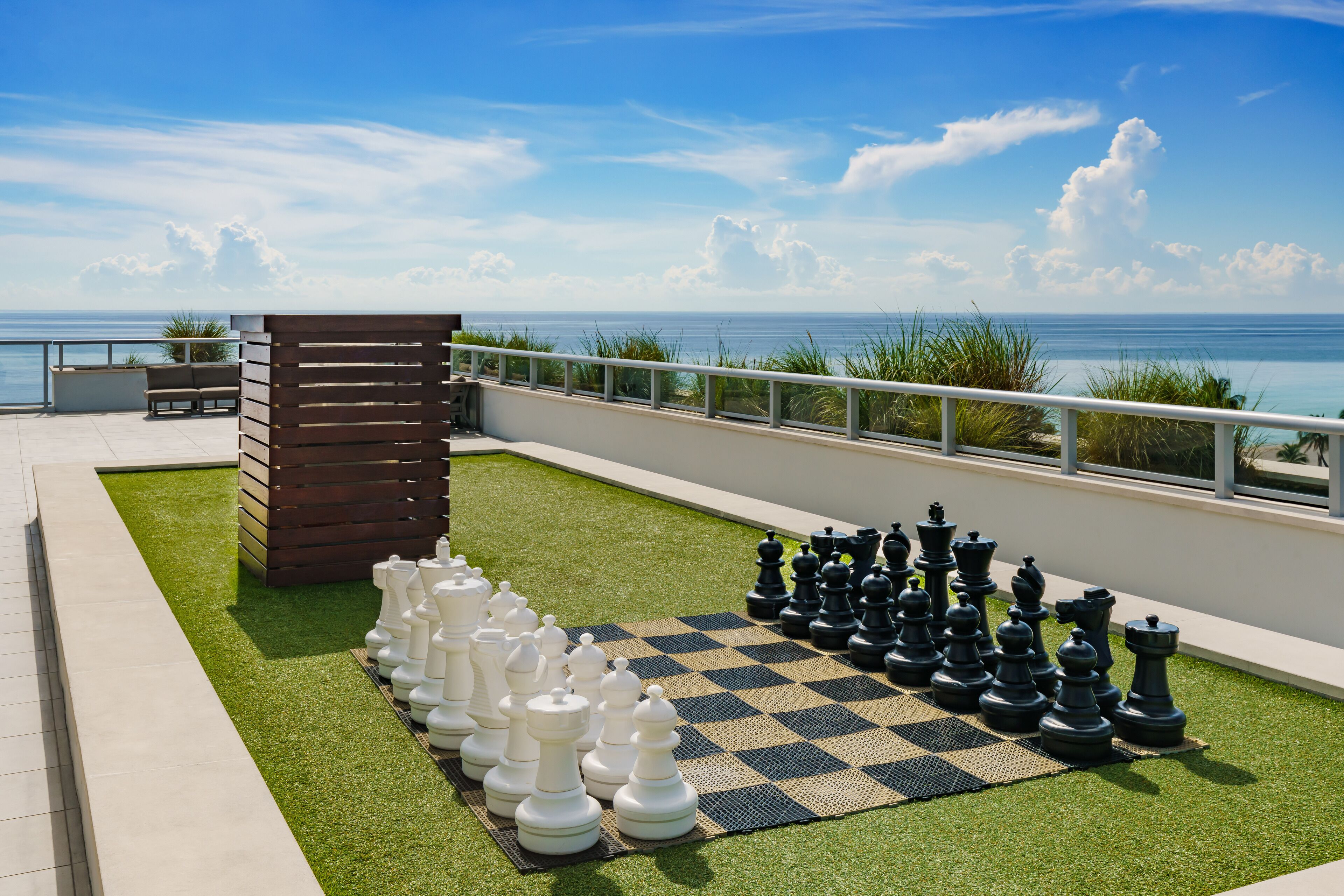A chessboard set up on a rooftop terrace with a view of the ocean.
