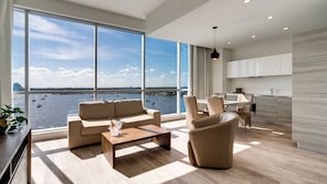 A spacious living area with a large window overlooking a body of water, a modern kitchen, and a dining area.