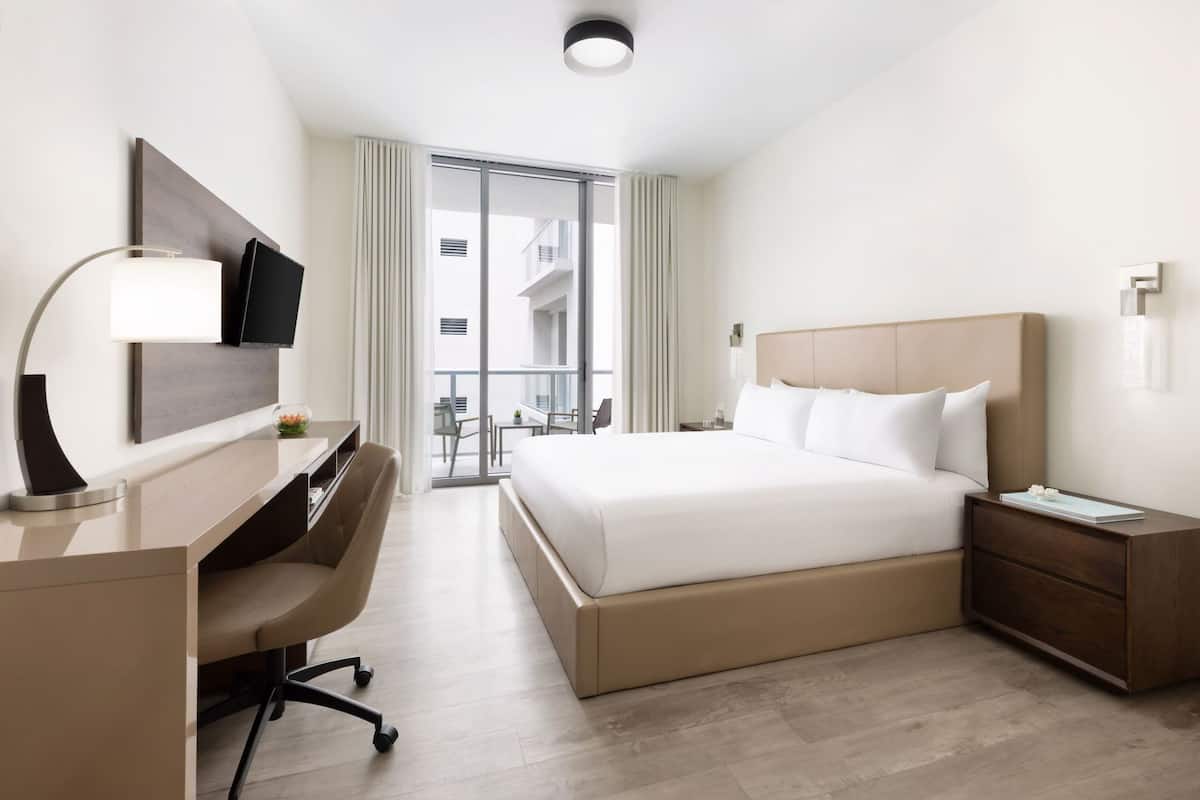 Une chambre d’hôtel équipée d’un lit, d’un bureau, d’une chaise, d’une télévision et d’un balcon avec vue.