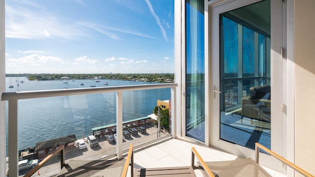 A balcony with a view of the water and boats, a glass door, and outdoor seating.