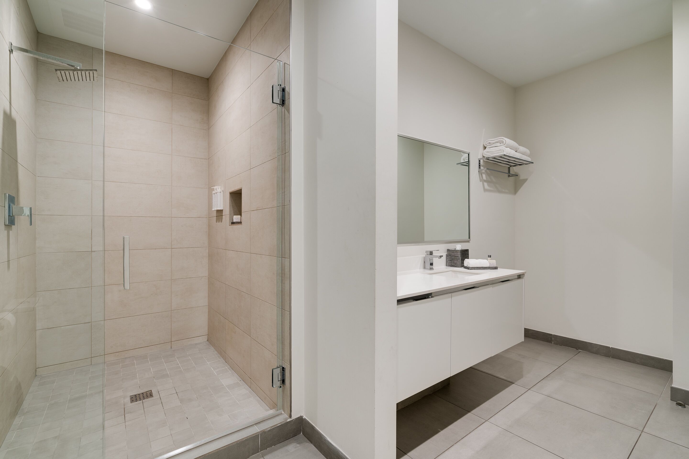 A modern bathroom with a glass-enclosed shower, a white sink, and a mirror above it.