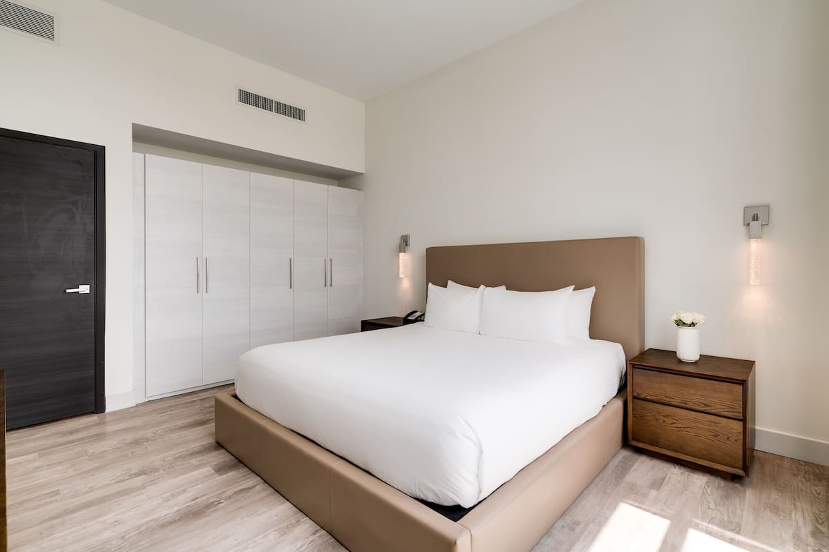 Une chambre à coucher moderne avec un grand lit, une table de chevet en bois, une porte sombre et une armoire blanche.