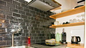 Een keuken met een zwarte tegelachterwand, roestvrijstalen apparatuur en houten planken met servies en glazen.