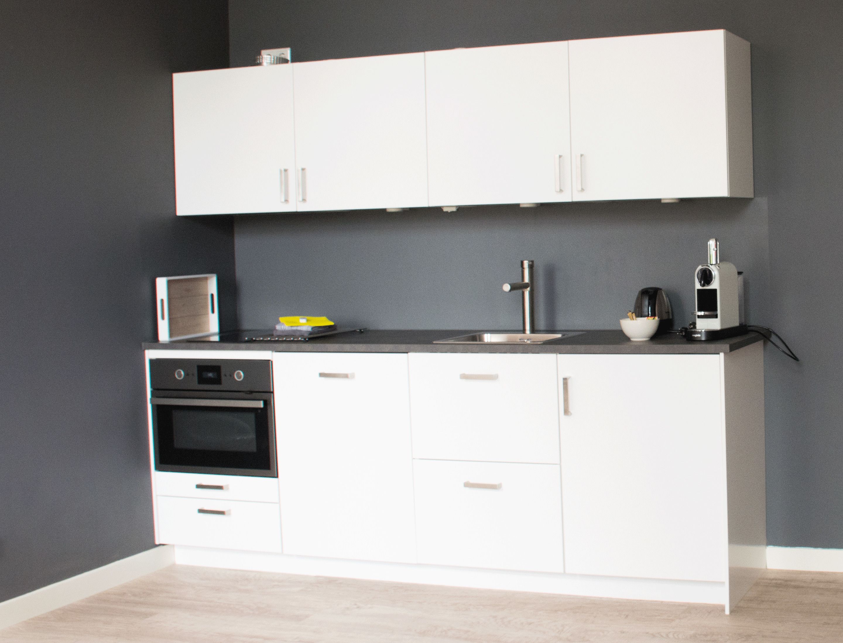 A modern kitchen with white cabinets, a built-in oven, a microwave, and a coffee maker.