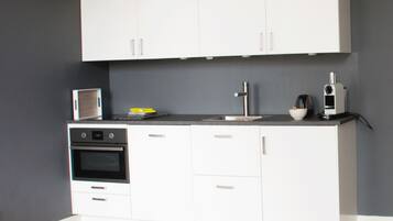 A modern kitchen with white cabinets, a built-in oven, a microwave, and a coffee maker.