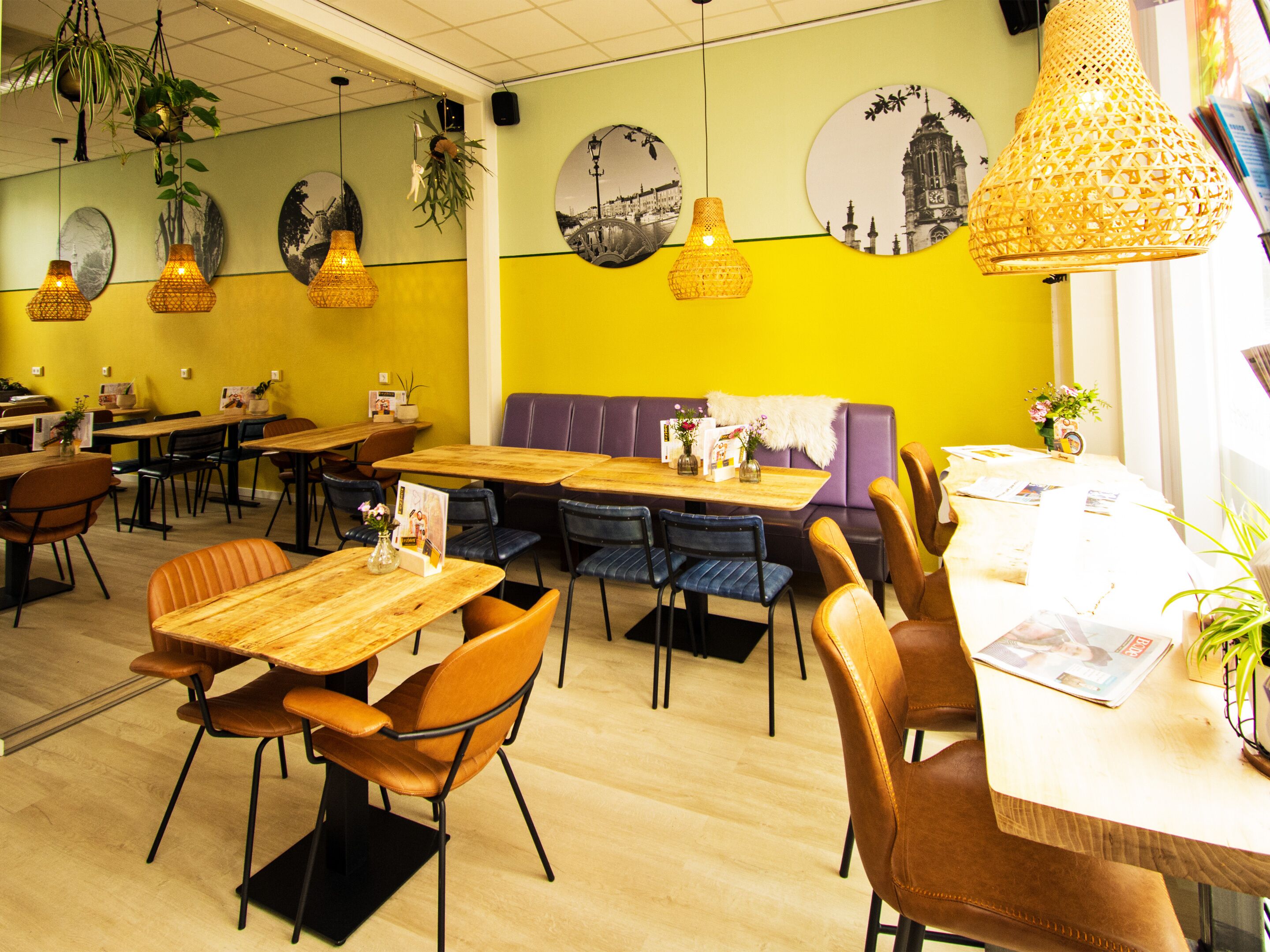 Un restaurante con mesas y sillas de madera, un asiento acolchado púrpura y lámparas colgantes.