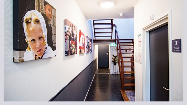 Un pasillo con una escalera, una puerta con la etiqueta “1” y una pared decorada con varios cuadros enmarcados.