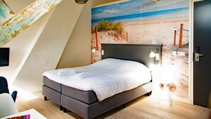 Een slaapkamer met een bed, een bureau en een stoel. Op de muur is een strandfries te zien.