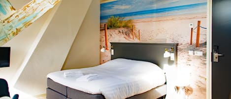 A bedroom with a bed, a desk, and a chair. There is a beach mural on the wall.