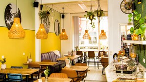 Un interior de restaurante con varias mesas y sillas para comer, plantas colgantes y un mostrador con productos alimenticios.