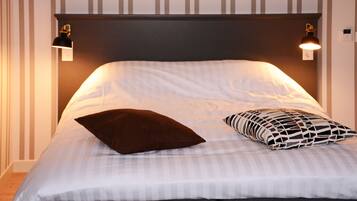A neatly made bed with striped bedding, two wall-mounted reading lamps, and a dark brown pillow.