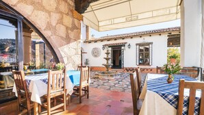Eine Terrasse im Freien mit Holztischen und -stühlen, einer Steinmauer und einem gefliesten Boden.