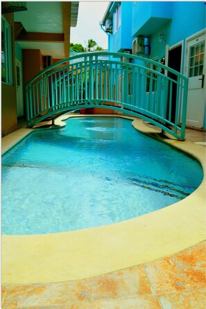 A swimming pool with a curved bridge, surrounded by a tiled deck and a building with a blue exterior. - Ella's Park View Townhouse Crown Point (Crown Point)