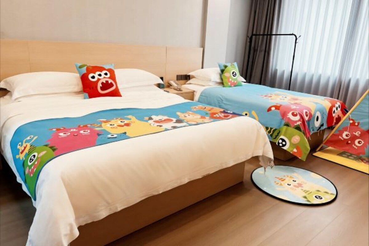 A hotel room with a large bed, two bedside tables, a bedside lamp, a window with curtains, and a small round rug.