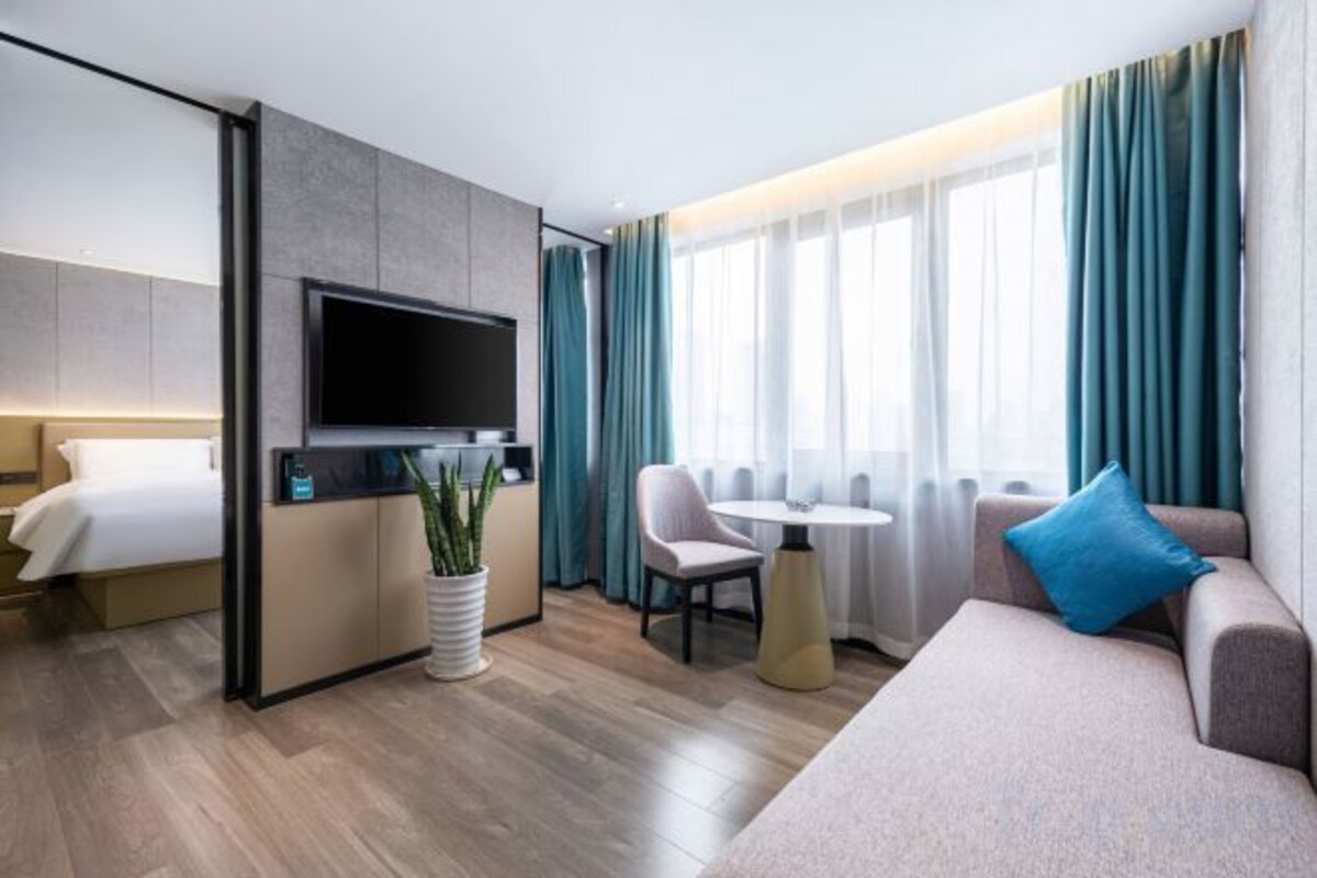 Une chambre d’hôtel avec un lit, une télévision, un coin salon et une fenêtre avec des rideaux.