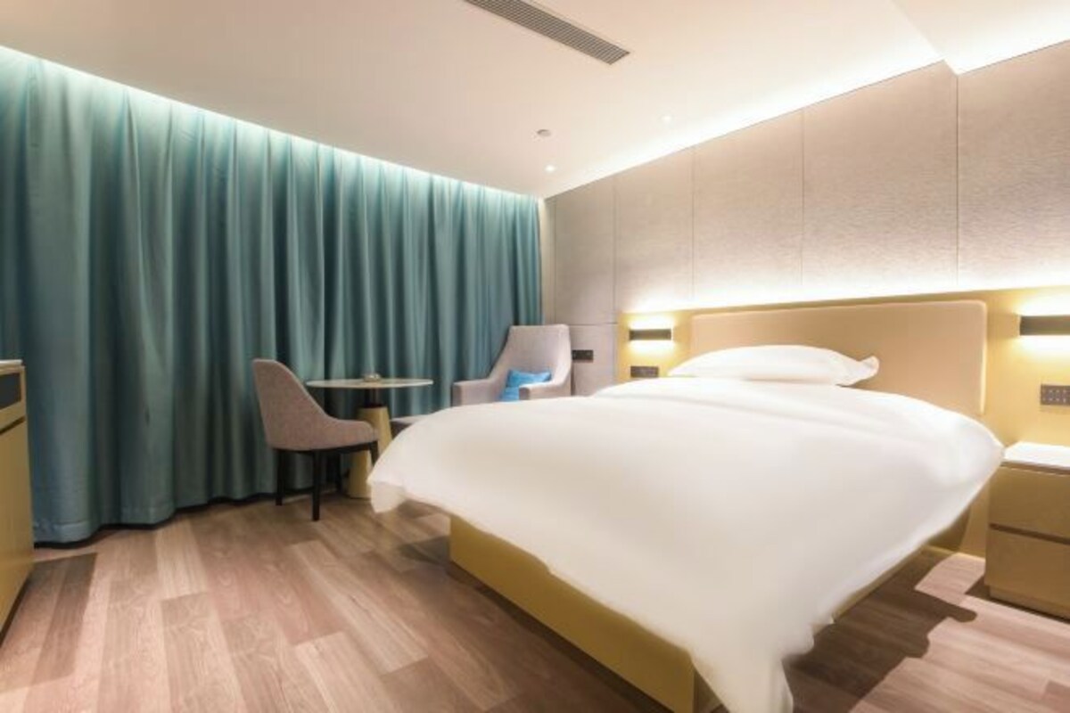 A modern hotel room with a large bed, a desk, a chair, and a curtain.