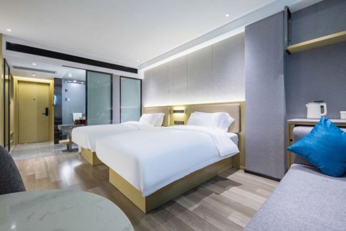 A modern hotel room with a large bed, bedside tables, a seating area, and a bathroom visible through a glass door.