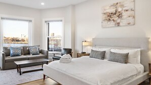 Una habitación de hotel moderna con una cama grande, un sofá, una mesa de centro y vistas a la ciudad.