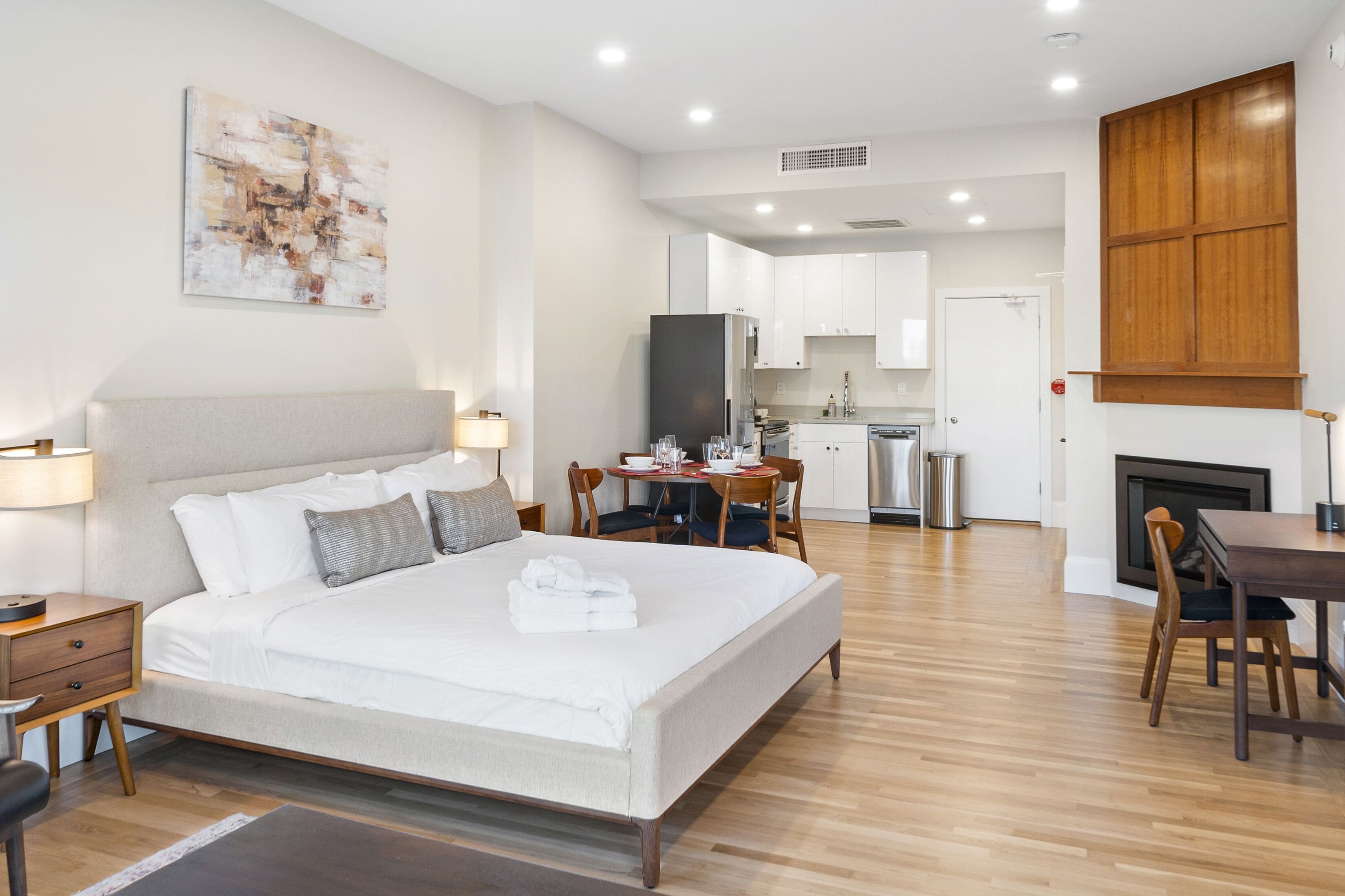 A modern hotel room with a large bed, a dining area, and a kitchen.