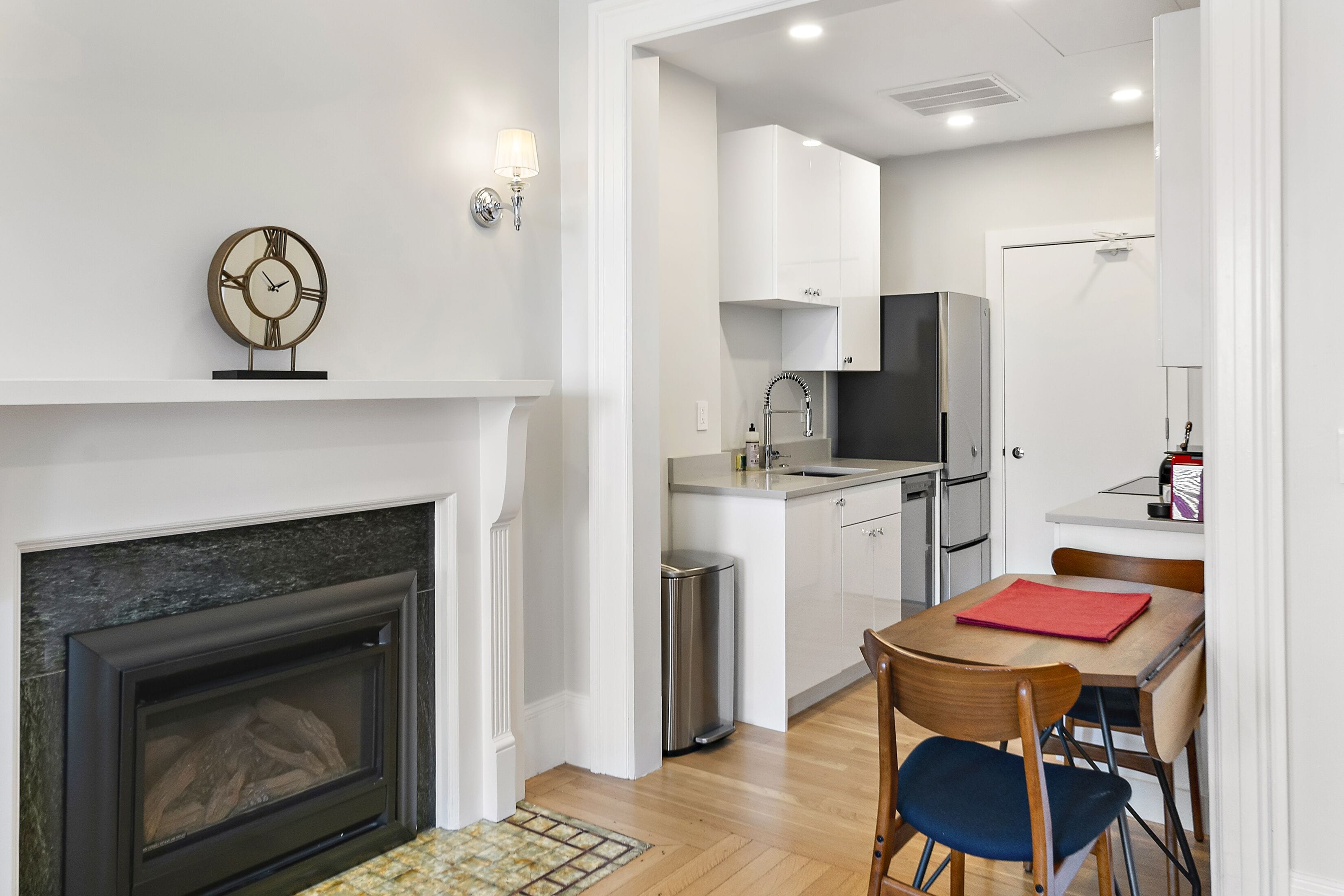A modern kitchen with white cabinets, a stainless steel refrigerator, and a dining area with a wooden table and chairs.