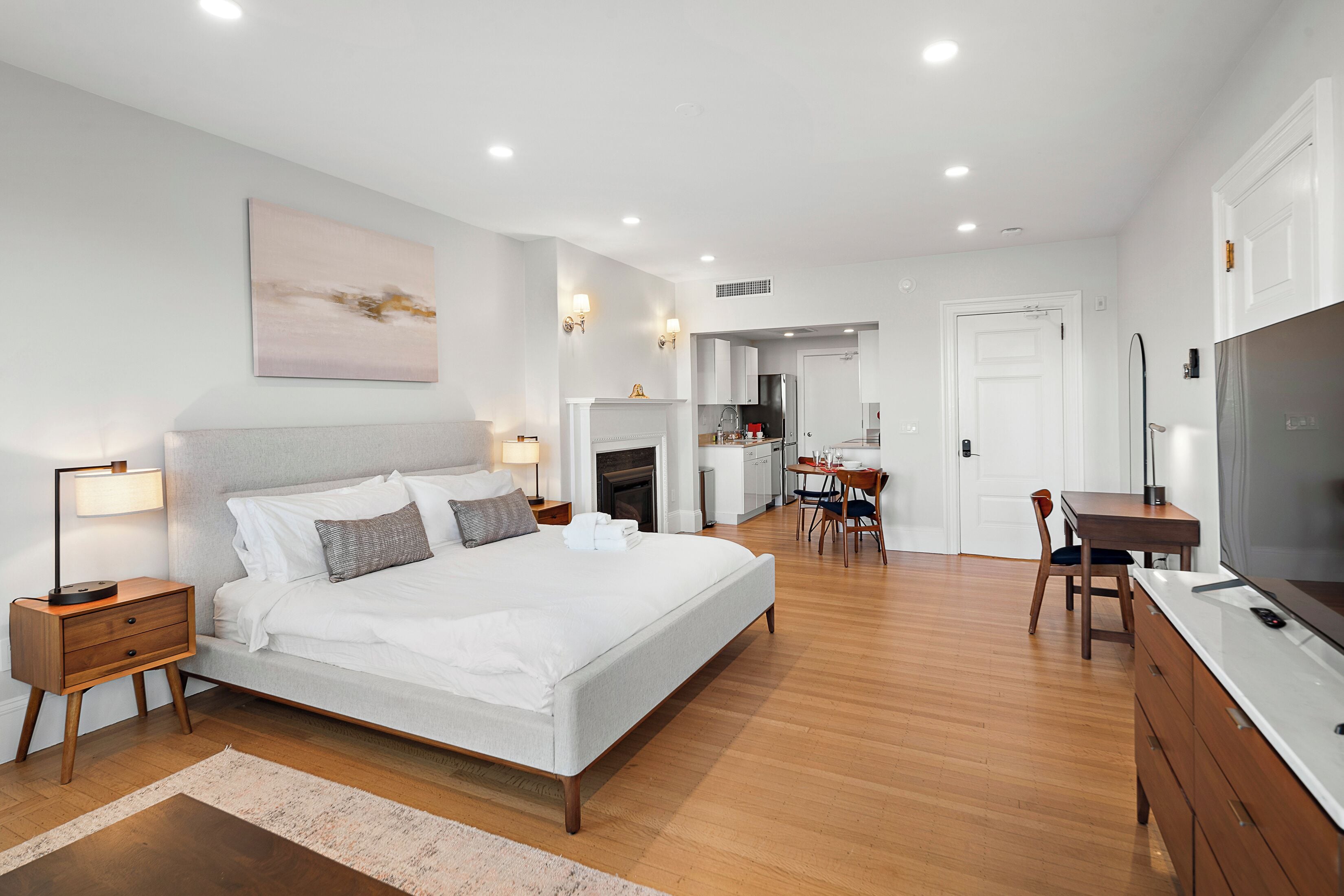 A modern bedroom with a large bed, bedside tables, a desk, and a television.