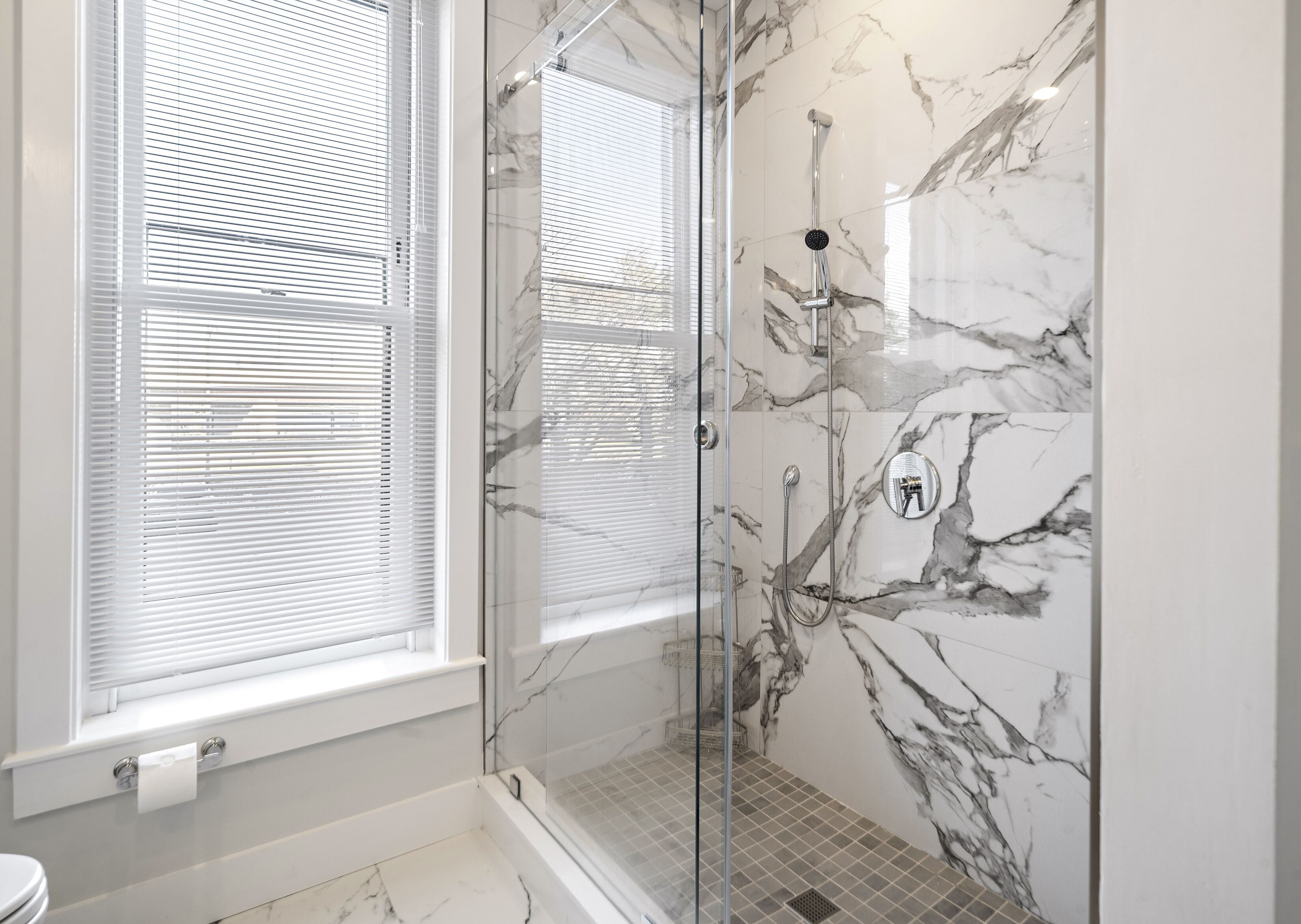 Une salle de bain moderne dotée d’une douche à parois de verre, de murs en marbre et de toilettes avec un porte-rouleau de papier toilette blanc.