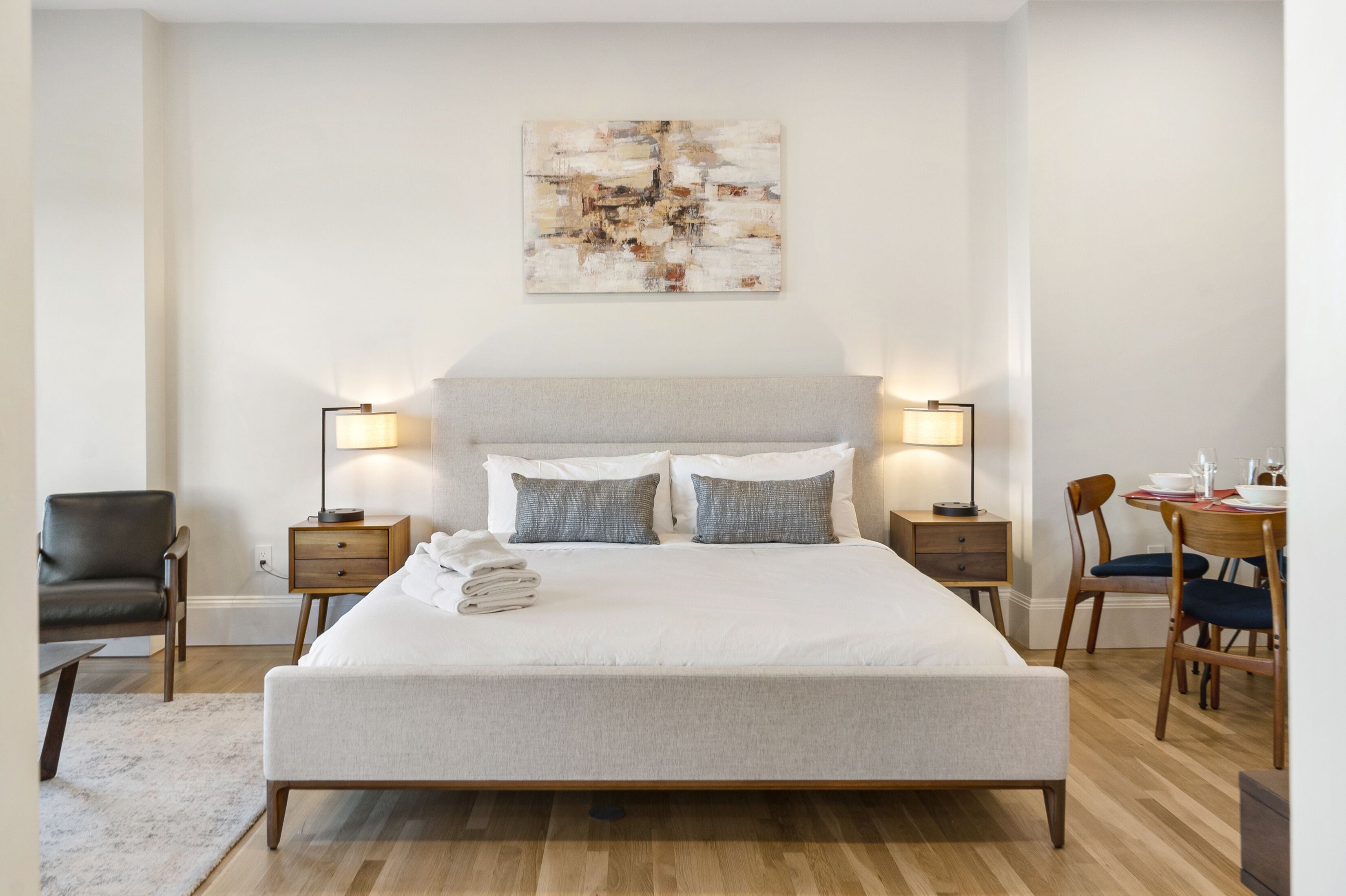 A neatly arranged bedroom with a large bed, bedside tables, a chair, and a dining area.