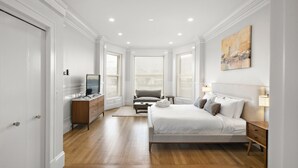 Un dormitorio moderno con una cama grande, un escritorio con computadora, una silla y un televisor.