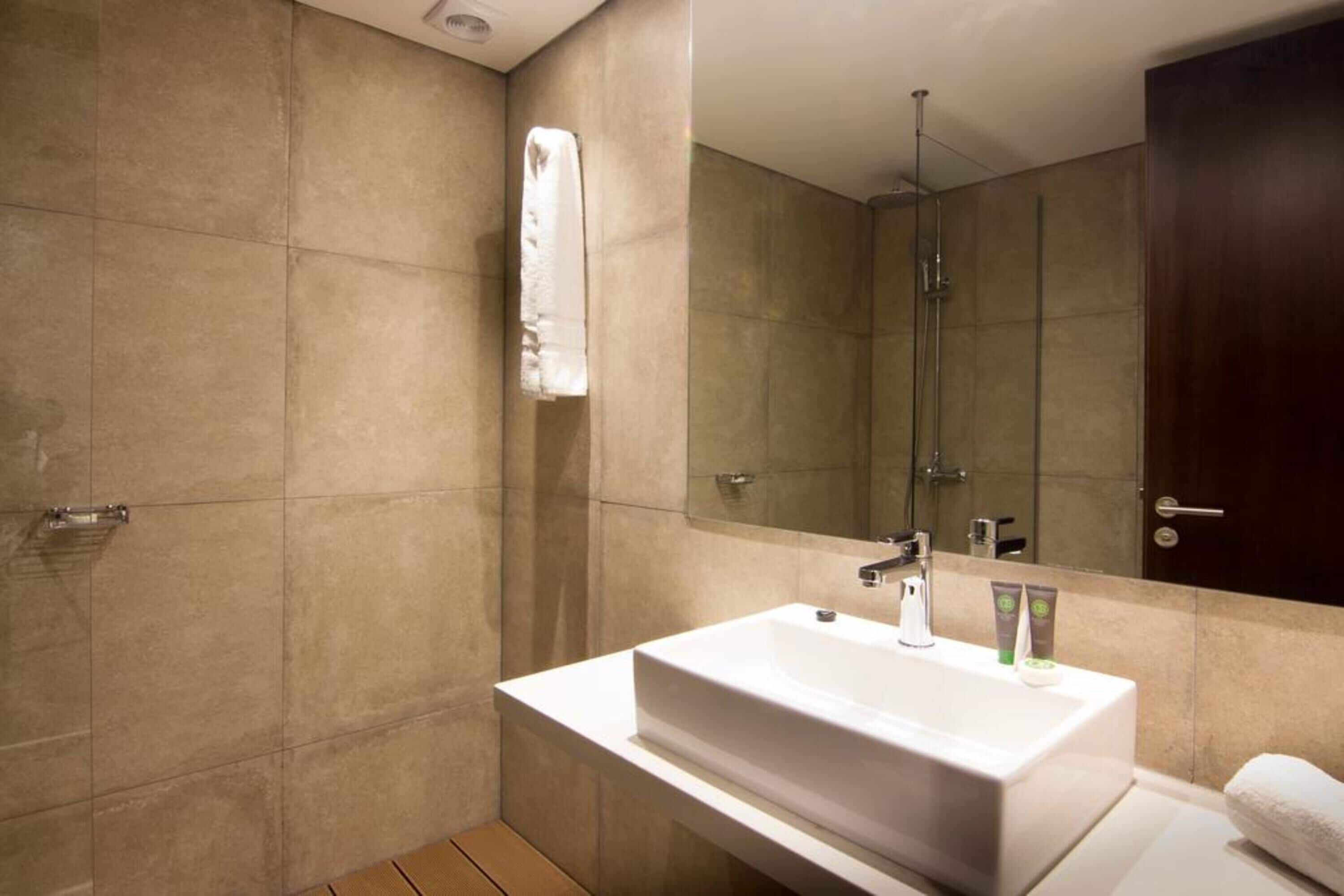 A modern bathroom with a large mirror, a white sink, and a shower area.