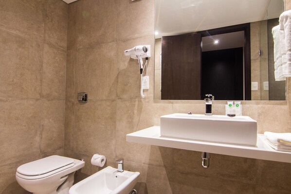 A modern bathroom with a toilet, bidet, sink, and a hairdryer mounted on the wall. - Hotel Ciudadano Suites (Montevideo)