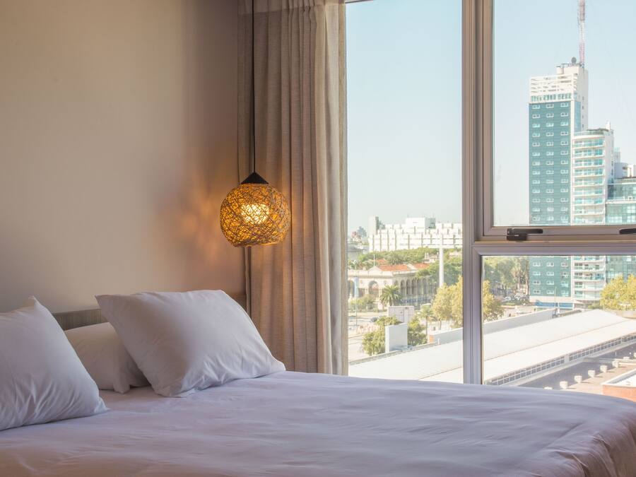 Una habitación de hotel con una cama grande, una ventana con vista a la ciudad y una lámpara de pared decorativa.