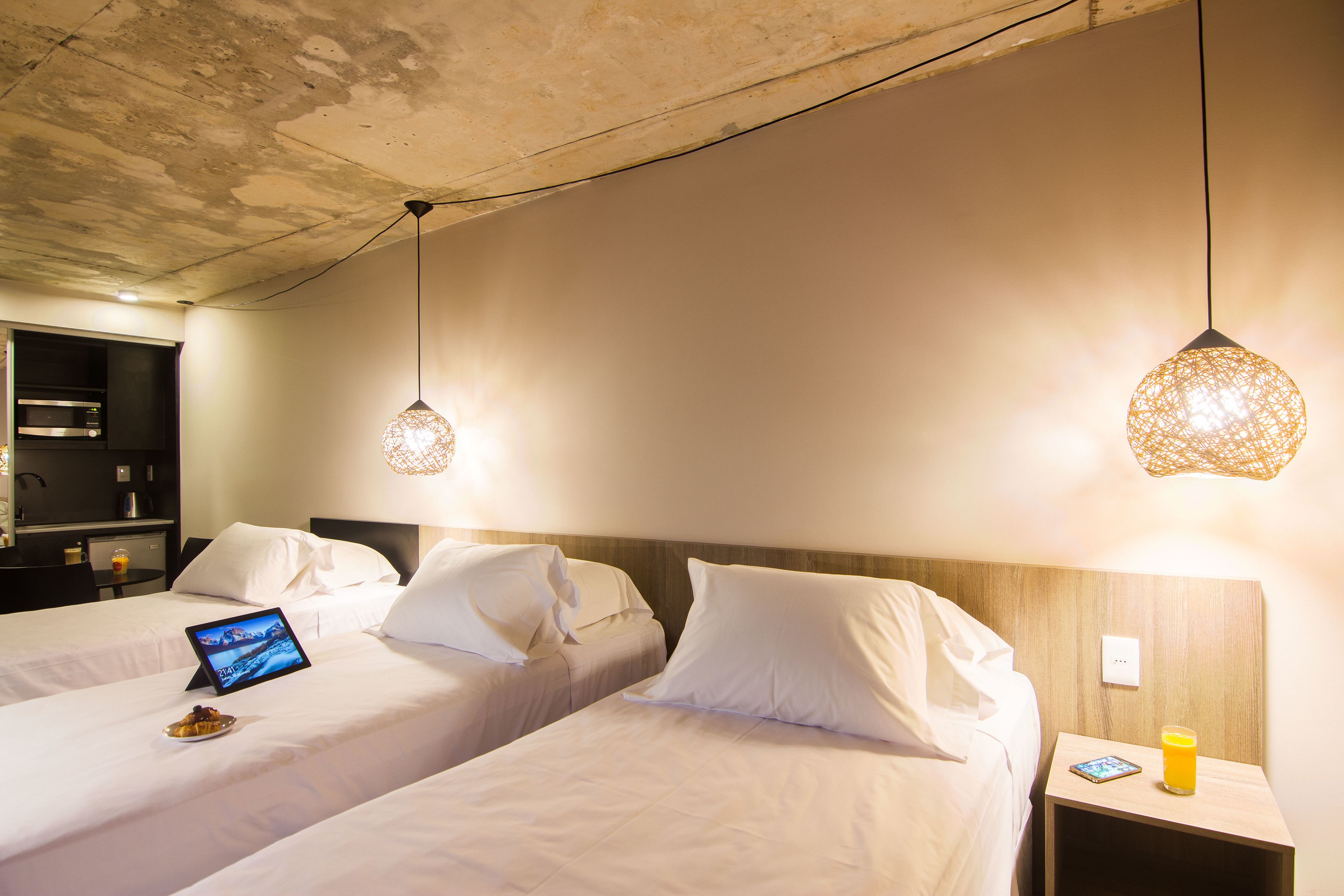 A hotel room with two beds, a bedside table with a lamp, and a tablet on one bed.
