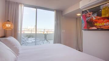 Ein Hotelzimmer mit Bett, Fernseher, einem Balkon mit Tisch und Stühlen sowie Blick auf die Stadt.